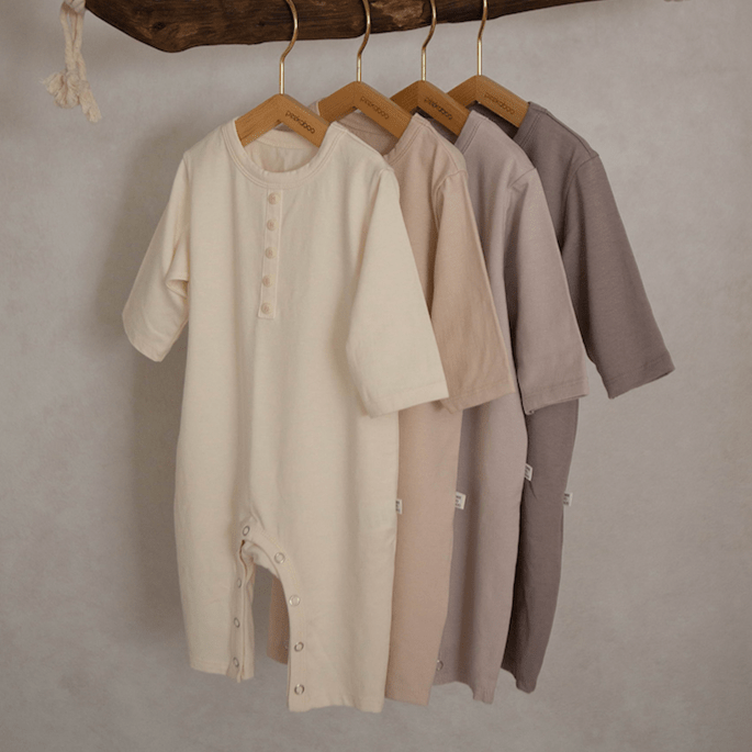 Peekaboo Peter sleepsuits in soft neutral tones hanging on wooden hangers