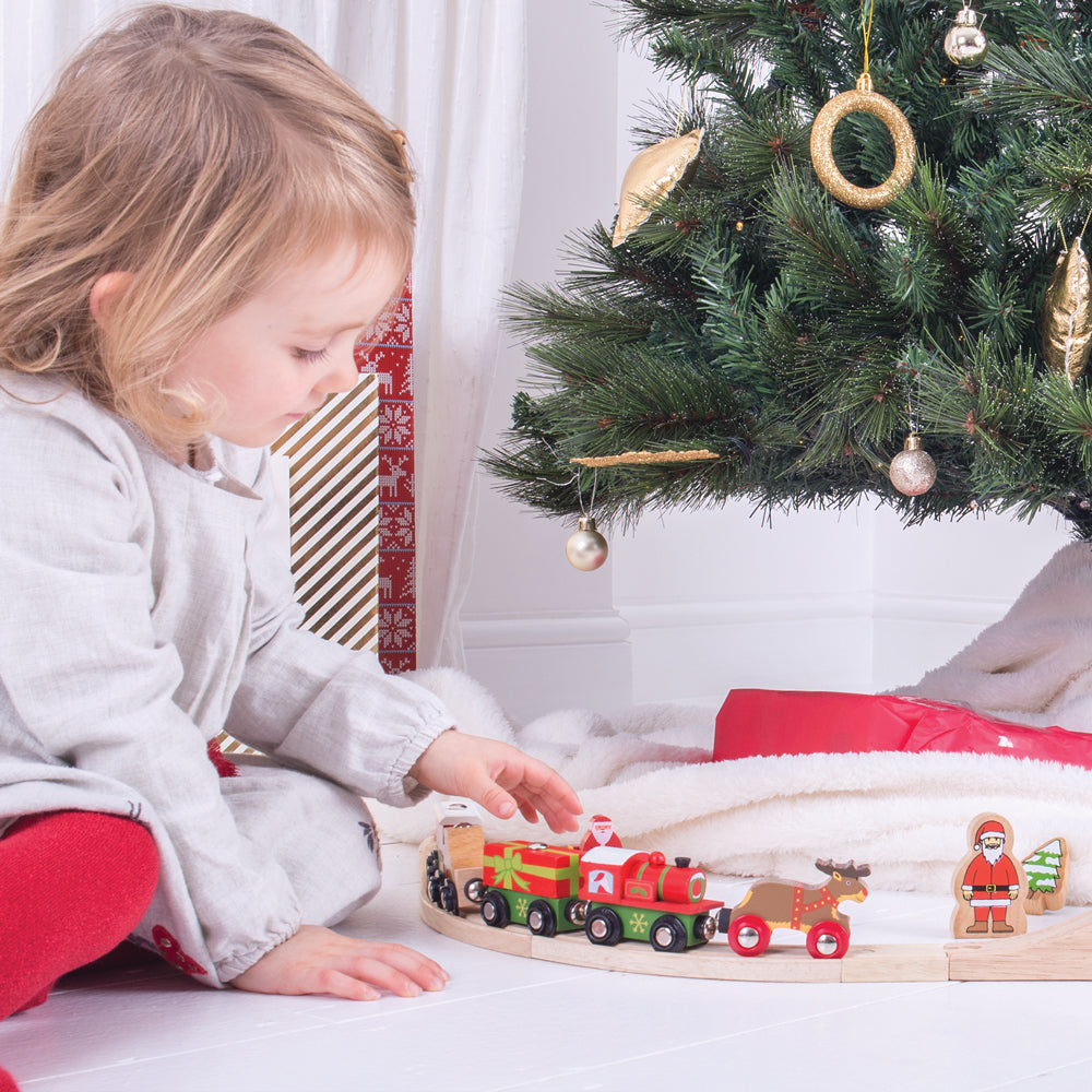 Child playing with the Bigjigs Rail Christmas wooden train beside a Christmas tree