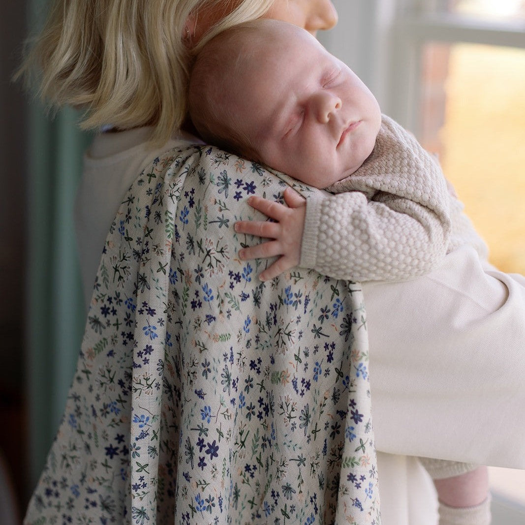 Parent holding a sleeping baby in a Wildflower print organic swaddle muslin