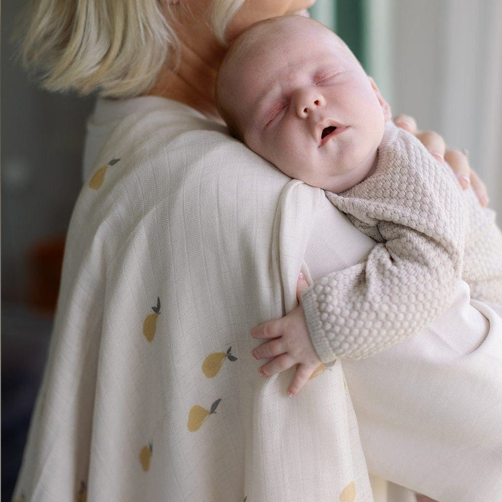 Parent holding a sleeping baby in a Pears print organic swaddle muslin