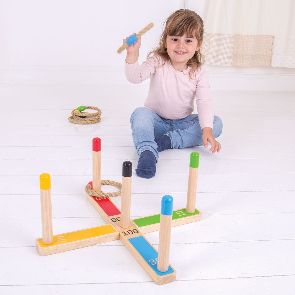 Girl playing the Bigjigs Wooden Quoits Game indoors, throwing a rope ring at the pegs