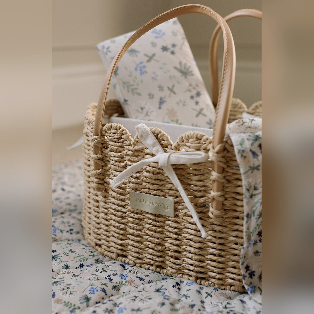 Ralphie Bear scallop edge nappy caddy holding a muslin and changing essentials on a floral nursery rug
