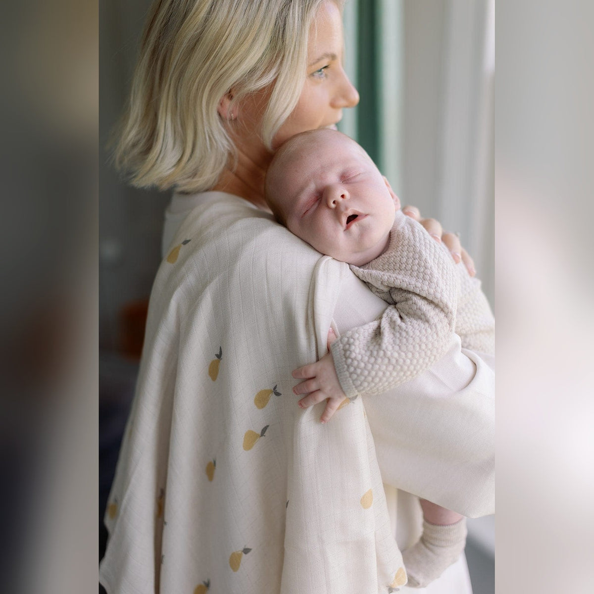Parent holding a sleeping baby in a Pears print organic swaddle muslin